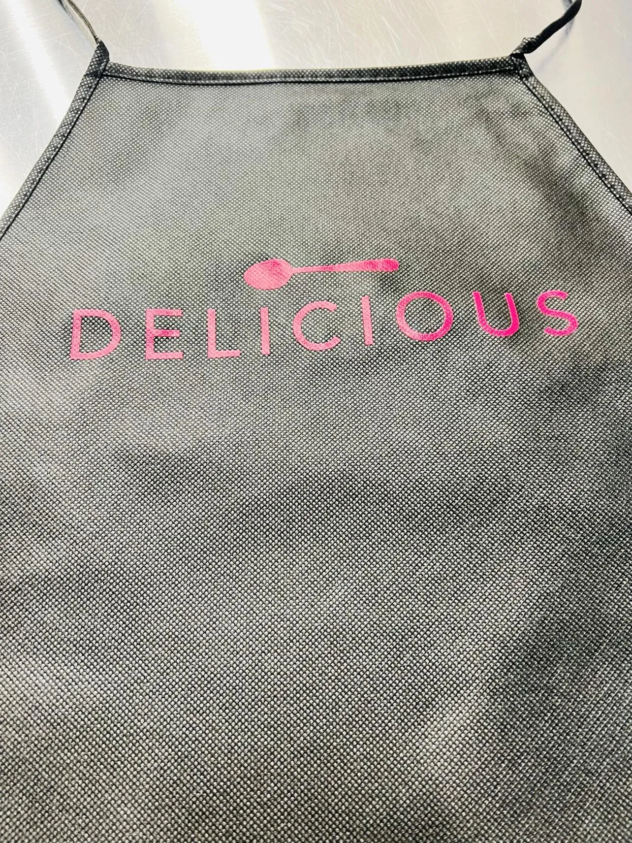 New Debco non woven Apron in Black with Pink Print "Delicious" on front! Tie closure, one size fits all! Winner can buy more at winning bid!